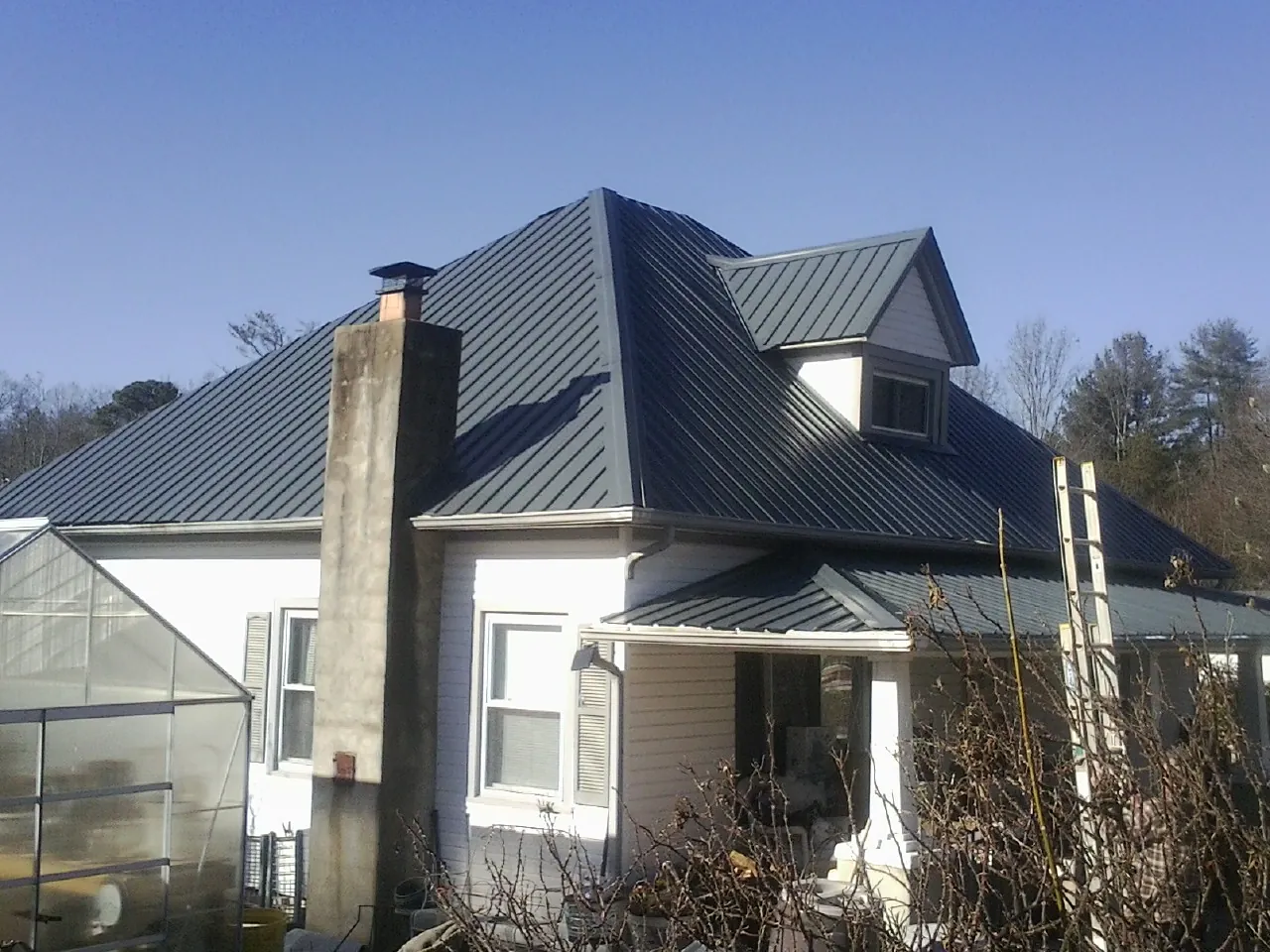 Dark blue standing seam metal roof on a white farmhouse with dormer — Slate & Tile Roof Repair by Roofing Brothers in Cashiers