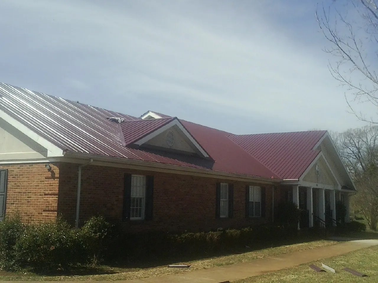 Red metal roof with gabled entries on a long brick building, from a Hail Damage Roof Repair job in Cashiers