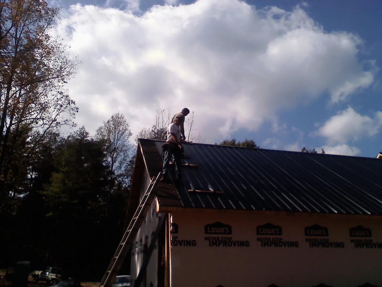 Roofer fastening dark metal panels high against a cloudy sky, from a Roof Inspection job in Cashiers
