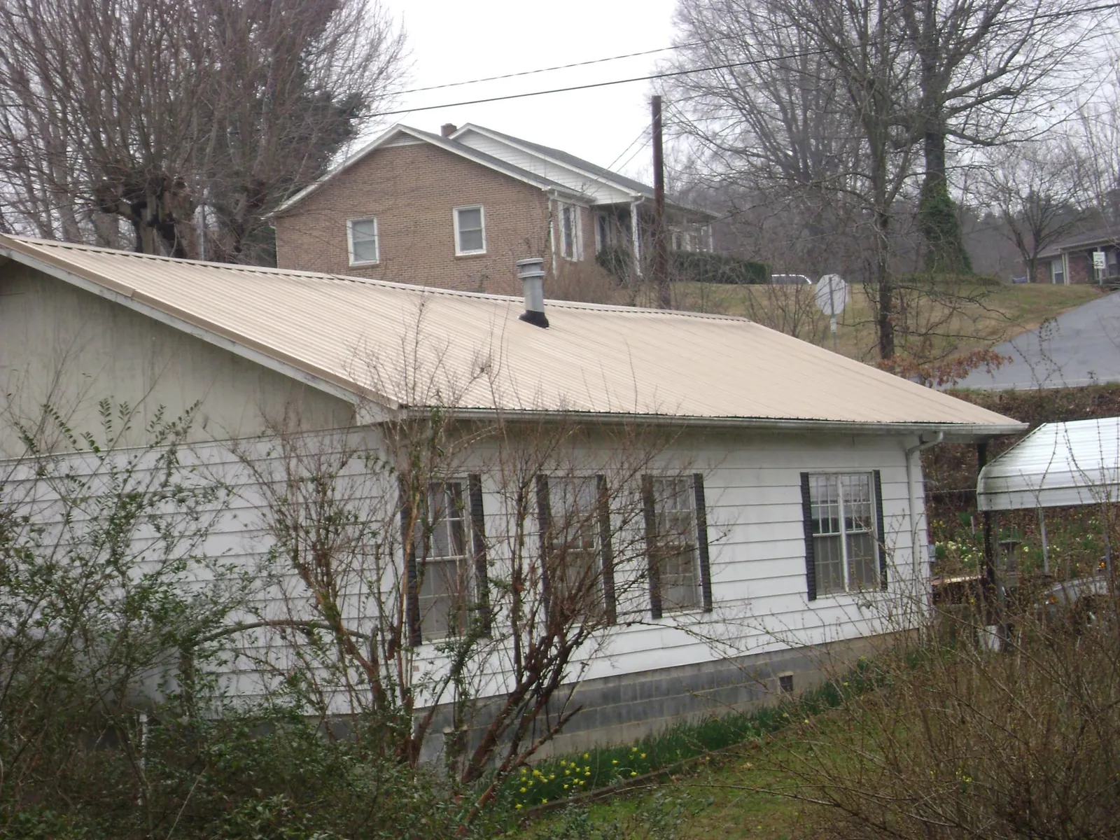 Tan metal roof on a white sided house set into a hillside — Commercial Roofing by Roofing Brothers in Cashiers