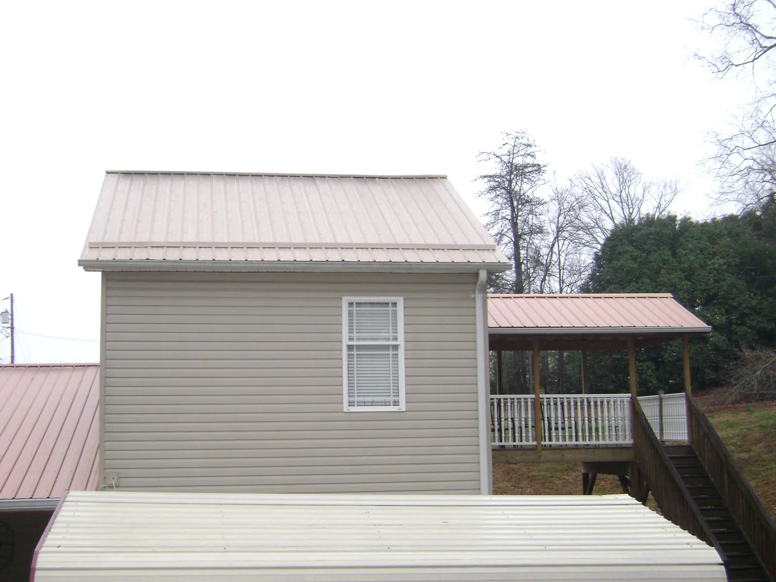 Tan metal roofs on a two story addition and attached porch, from a Roof Replacement job in Cashiers